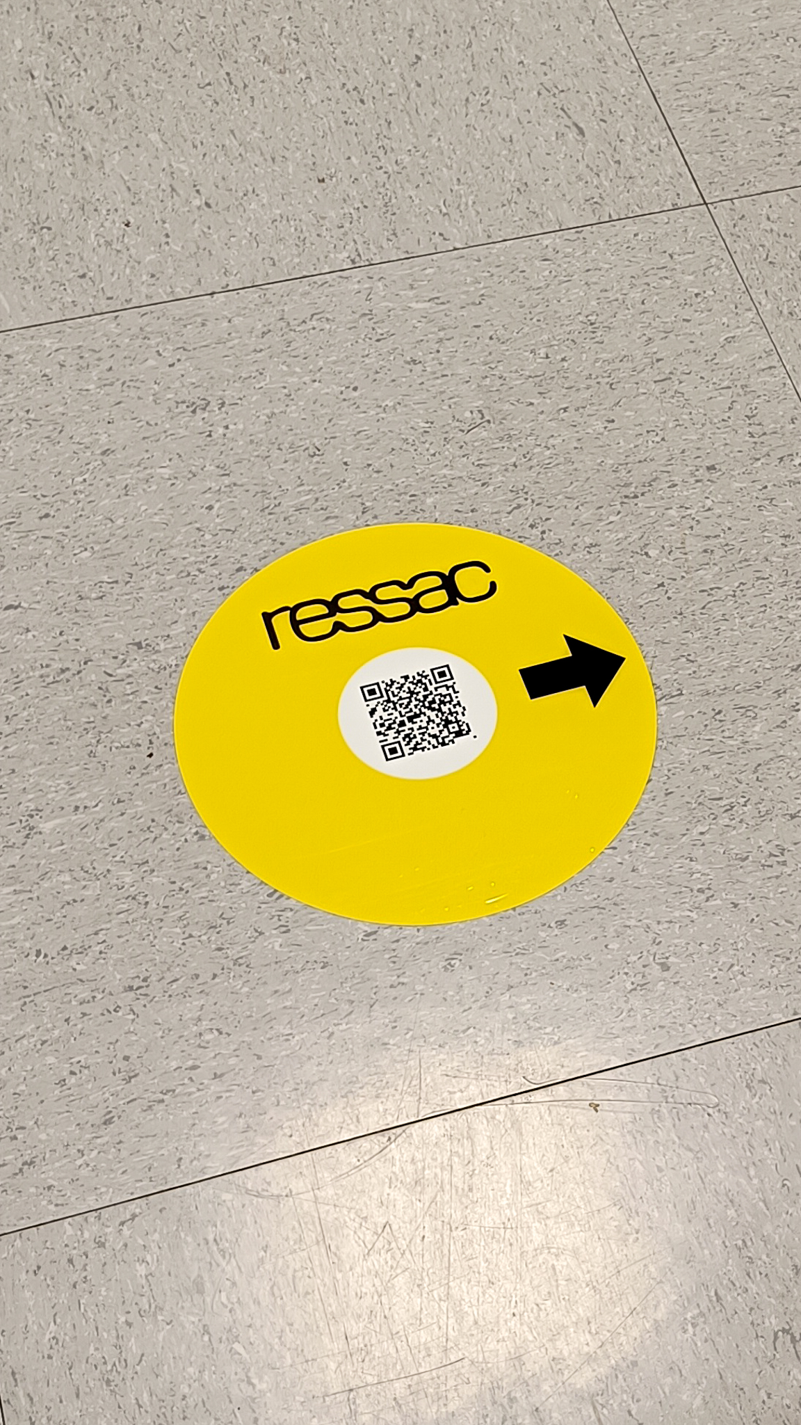 Autocollant au sol rond, jaune, avec le logo RESSAC noir, un QR code noir sur fond blanc et une flèche noire