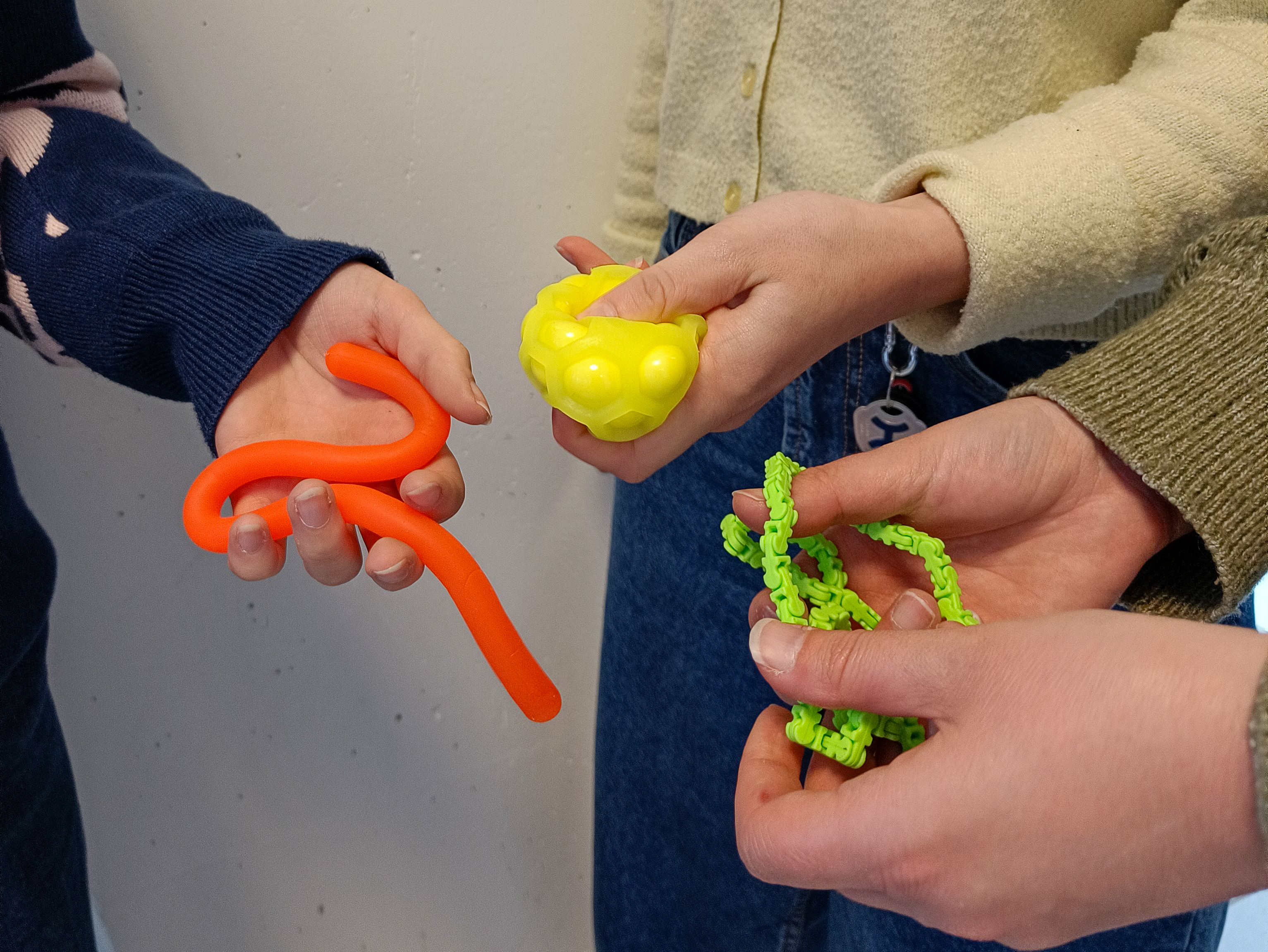 Trois paires de mains tenant chacune un stim toys différent.